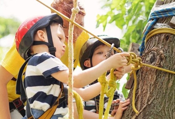 Deux enfants portant casques et harnais participent à une activité d'accrobranche en forêt.