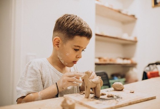 Un enfant fait de la poterie avec de l’argile sur une table en bois.