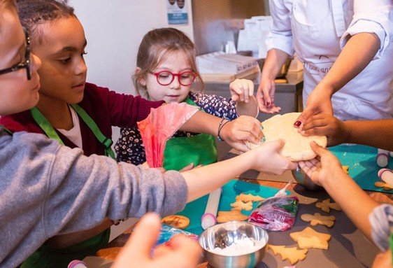 Des enfants participent à une activité de cuisine en groupe, manipulant des morceaux de pâte et des emporte-pièces sur une