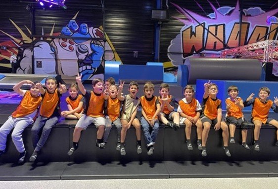 Groupe d’enfants en t-shirts orange assis sur un banc dans un parc anniversaire enfant île de france, fond coloré avec graffiti et structures de jeux couvertes.