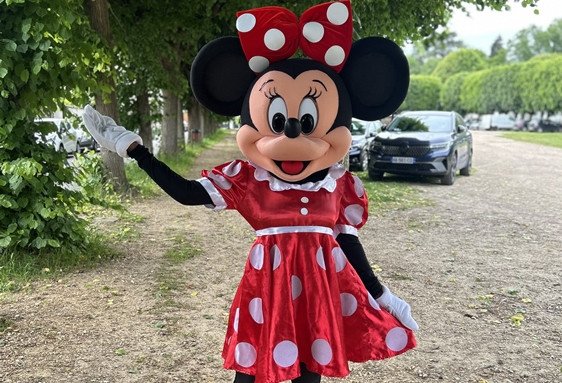 Personnage déguisé en Minnie Mouse saluant dans un chemin extérieur.