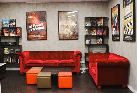 Salon cosy avec canapés rouges et ottomans colorés et posters au mur.