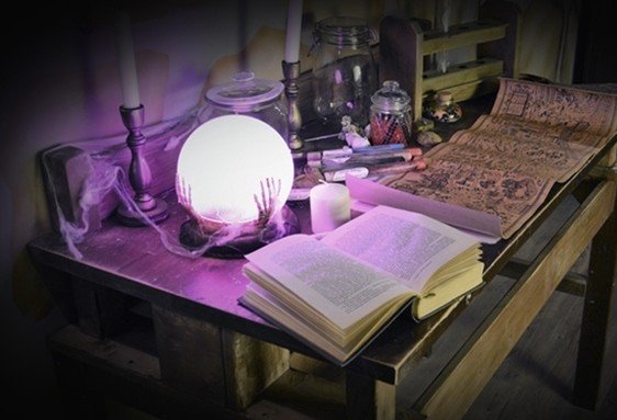 Table d’étude et objets de magie sur une surface en bois avec livre ouvert et globe lumineux.