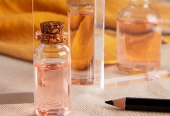 Vase en verre avec bouchon en liège et fiole contenant un liquide rose pâle, posé près d’un crayon noir.